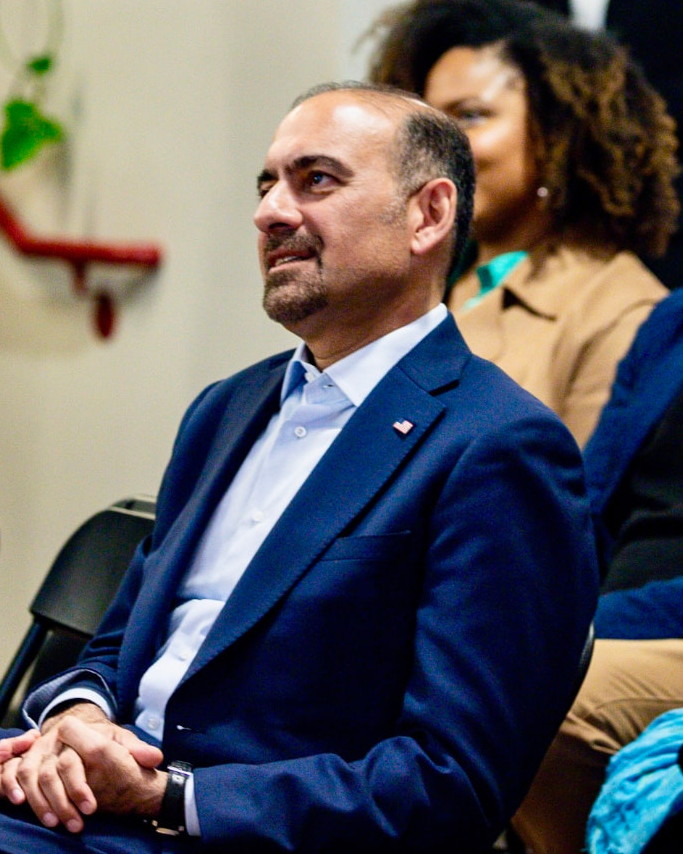 Dilawar Syed seated thoughtfully during a public gathering.